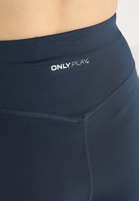 Leggings blu navy realizzati in tessuto elasticizzato, con un alto elastico in vita e il logo bianco 'ONLY PLAY' nella parte superiore. Texture liscia con cuciture piatte.