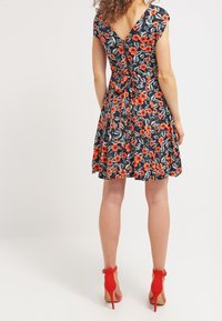 Květinové šaty s námořnickým pozadím, krátkými rukávy, V-výstřihem na zádech a zúženým pasem. Doplněné červenými vysokými podpatky.