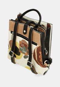 Sac à dos multicolore en matériau texturé doux avec des motifs noirs, bruns et jaunes. Il dispose de poignées doubles et de compartiments zippés.