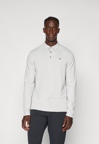 Camisa polo de manga longa em cinza claro com colarinho, placket de três botões e pequeno logótipo bordado no peito esquerdo. Textura suave.