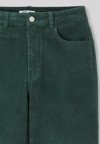Pantalon en velours côtelé vert avec une texture ribbed verticale. Comprend une poche avant et une fermeture à bouton en métal à la taille.