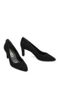 Tacones altos de mujer en ante negro con puntera puntiaguda y tacones de bloque de altura media, mostrados uno al lado del otro sobre un fondo blanco.
