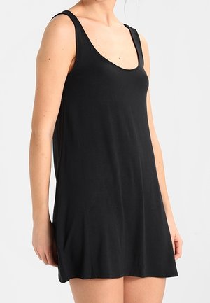 Mujer con un vestido negro de verano sin mangas y escote redondo, mostrada desde los hombros hasta la mitad del muslo sobre un fondo liso.