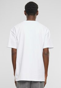 T-shirt blanc à manches courtes avec une coupe décontractée et un col rond. Fabriqué en coton, il présente une texture lisse et un design sobre sans graphiques visibles.