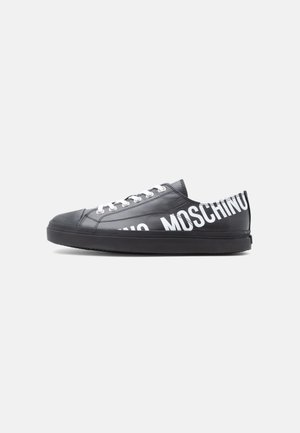 Zapatilla deportiva negra de corte bajo con cordones blancos y "MOSCHINO" impreso en grandes letras blancas a lo largo del lateral y el talón.