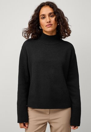 Schwarzer Strickpullover mit hohem Kragen, weiten Ärmeln und geripptem Saum. Die Textur ist weich und voluminös, ideal für lässige Outfits.