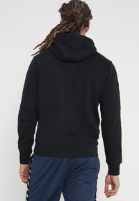 Felpa nera con cappuccio regolabile, polsini e orlo a coste. Caratterizzata da una texture liscia e da un design pulito e minimale.