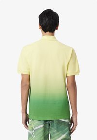 Polo shirt med en gul til grøn gradient, korte ærmer og en klassisk krave, lavet af blødt stof med en glat tekstur.
