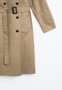 Beige Trenchcoat aus Baumwolle, mit einem doppelt knöpfbaren Design, schwarzen Knöpfen, einem Gürtel mit rechteckiger Schnalle und einer mittellangen Schnittführung.