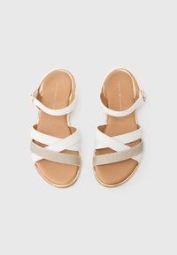 Hvite sandaler med kryssende stropper, gullakcenter og en glitrende sølvstrop. Glatt beige såle, justerbar ankelspenne. Klassisk design.