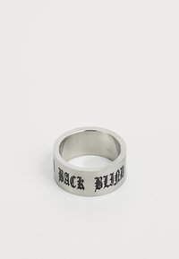 Sølvmetallring med flat bånddesign, med hevet svart skrift som leses "BACK BLIND." Glatt tekstur med matte overflate.