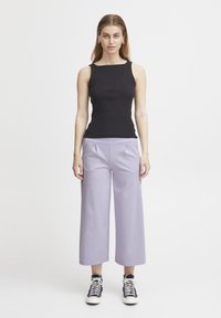 Zwart mouwloos topje met ribbeltextuur, gecombineerd met licht lila wijde broek. Schoeisel: zwart-wit hoge sneakers.
