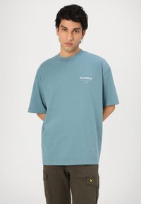 T-shirt en coton bleu clair à manches courtes et col rond. Présente un petit logo blanc sur la poitrine. Associé à un pantalon cargo olive.