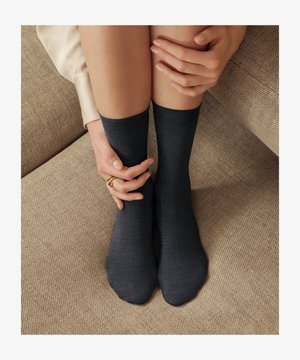 Sötétszürke boka zokni puha anyagból, bordázott szegélyekkel és sima felülettel, amelyet kezek viselnek, amelyek egy texturált felületen nyugszanak.