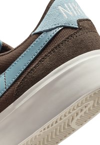 Brun sneakers med lyseblå accenter, struktureret ruskind og tekstiloverdel, gummisål med mønstrede riller og broderet logodetalje.
