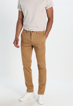 Beige chinos van katoen, met een recht model, voorzakken en een knoopsluiting. Gepaard met een lichtgrijze T-shirt en witte sneakers.