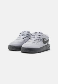 Sneakers Nike Air Force 1, szare skórzane wierzchy, czarne akcenty, okrągły nos, sznurowane zapięcie, teksturowana gumowa podeszwa z wzorzystym bieżnikiem.