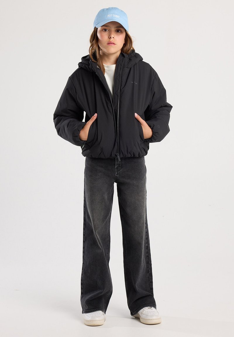 Black puffer jacket with hood, zip closure, and elastic cuffs. Worn over a light shirt and paired with faded black wide-leg jeans and white sneakers. Light blue cap.