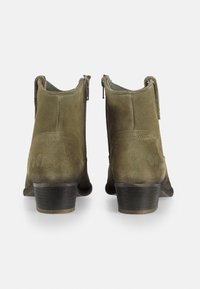 Botines de ante verde oliva con tacón bajo apilado y cierre de cremallera lateral. Presentan una textura suave y un sutil detalle del logo de mariposa.