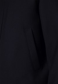 Tessuto blu navy con una superficie liscia, dotato di una tasca laterale e un design su misura. I punti di cucitura sono ordinati e discreti.