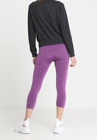 Leggings morados con un patrón, de diseño ajustado, combinados con un sudadera negra texturizada y zapatillas blancas.