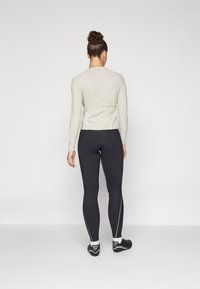 Lichtbeige langemouwen top met een fitted ontwerp, gecombineerd met zwarte leggings met reflecterende accenten en een gladde textuur.