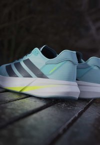 Baskets de course bleu clair avec des rayures gris foncé, matériau supérieur texturé et un accent jaune sur le talon. Dotées d'une semelle blanche épaisse.