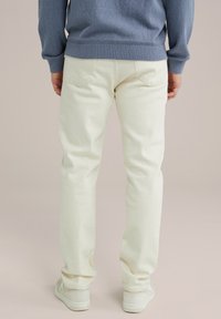 Jeans blancos de algodón con un corte recto, que presentan bolsillos traseros, combinados con zapatos claros y un suéter azul texturizado.