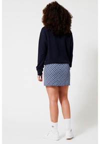 Marinblå tröja och mönstrad blå minikjol, kombinerat med vita sneakers och strumpor. Tröjan har en avslappnad passform; kjolen har en geometrisk design.