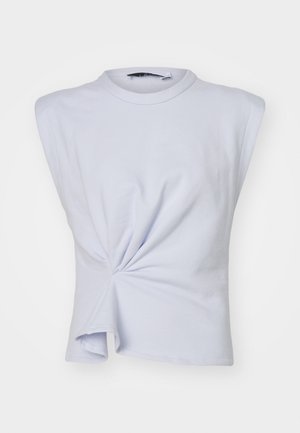 Nainen, jolla on yllään hihaton valkoinen kierretty etutoppi, mustat kapeat housut, joissa on kerätyt nilkat, ja mustat avokärkiset korkokenkä-mule-kengät.
