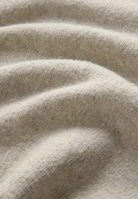 Svetlo béžová tkanina s jemnou, textúrovanou väzbou, ukazujúca mierne záhyby a hladký povrch, naznačujúca teplo a pohodlie.