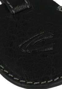 Sandale en cuir noir avec une surface texturée, des coutures grises et un logo en relief discret sur la sangle avant.