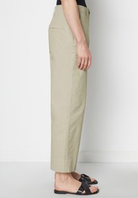 Lichte khaki broek met een relaxte pasvorm, rechte pijpen en een omgeslagen zoom, in combinatie met platte zwarte sandalen. De stof lijkt glad.