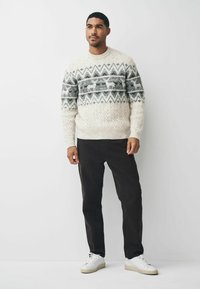 Krümeliger Strickpullover mit grauem Fair-Isle-Muster, das Rentiere zeigt, kombiniert mit schwarzen Hosen und weißen Sneakers. Grobe Textur, Rundhalsausschnitt.