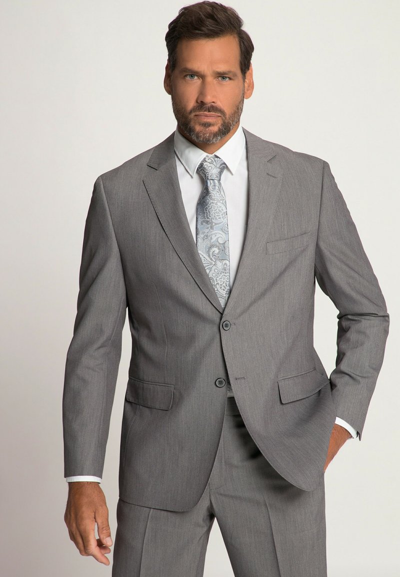 Completo grigio slim fit con giacca a due bottoni, taschino singolo sul petto e pantaloni abbinati. Camicia bianca e cravatta a righe blu chiaro.
