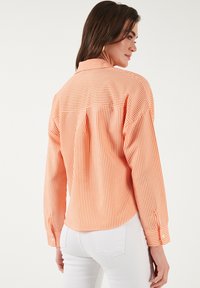 Oranje en wit gestreepte button-up shirt met een rugplooitje, lange mouwen en manchetten. Gemaakt van lichte stof.