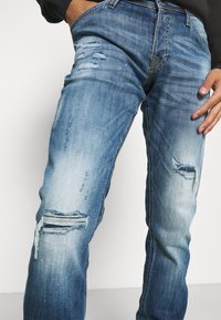 Vaaleansiniset farkut, joissa on haalistunut viimeistely, repaleiset yksityiskohdat molemmissa polvissa ja klassinen viisitaskuinen malli.