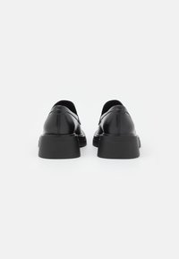 Chaussures en cuir noir avec un bout rond et une semelle noire épaisse et texturée. Finition lisse. Aucun élément métallique ni motif visible.