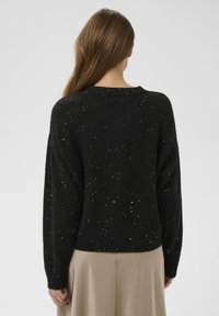 Fekete pulóver laza szabással, ezüstös díszítéssel eloszlatva. Bordázott mandzsetta és szegély, kerek nyakkivágás, puha tapintás.