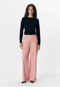 Maglia nera a maniche lunghe abbinata a pantaloni larghi a righe rosse e bianche; il modello indossa tacchi a punta neri.
