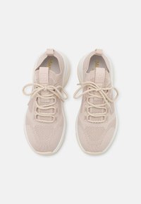 Zapatillas deportivas beige con parte superior de punto, suela de goma, cordones en la parte delantera y un diseño texturizado. Cuenta con una lengüeta y acentos de logotipo elevados.