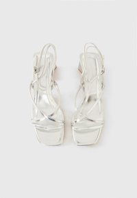 Silberne, blockabsatzpumps mit mehreren gekreuzten Riemen, quadratischer Zehenpartie und glänzendem Lackfinish. Strukturierte Sohle für besseren Halt.