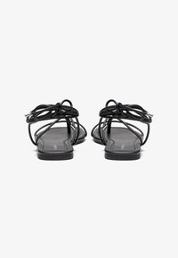 Sorte flate sandaler med tynne stropper, med en knyttet design foran og en glatt, rektangulær såle.