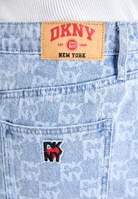 Jean en denim bleu clair avec une étiquette logo DKNY sur la ceinture et un petit logo brodé sur la poche arrière. Design texturé.