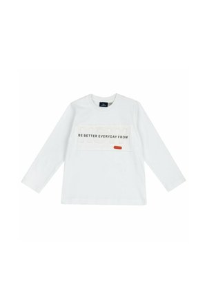 Camicia bianca a maniche lunghe con la scritta "BE BETTER EVERYDAY FROM" e grande scritta in rilievo "NOW" sul petto, con un piccolo dettaglio rettangolare arancione.