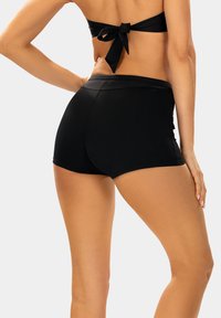 Czarny stanik bikini z zawiązaniem z tyłu oraz czarne kąpielówki z wysokim stanem. Gładki, elastyczny materiał z dopasowanym krojem. Brak widocznych wzorów lub akcentów.