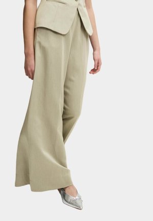 Pantalones de pierna ancha en un tono oliva claro, confeccionados en una tela ligera, con una textura suave y un corte ajustado, combinados con bailarinas plateadas de punta.