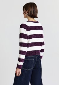 Purple and white striped sweater with a ribbed texture, round neckline, and cropped hem. Paired with dark denim wide-leg pants.