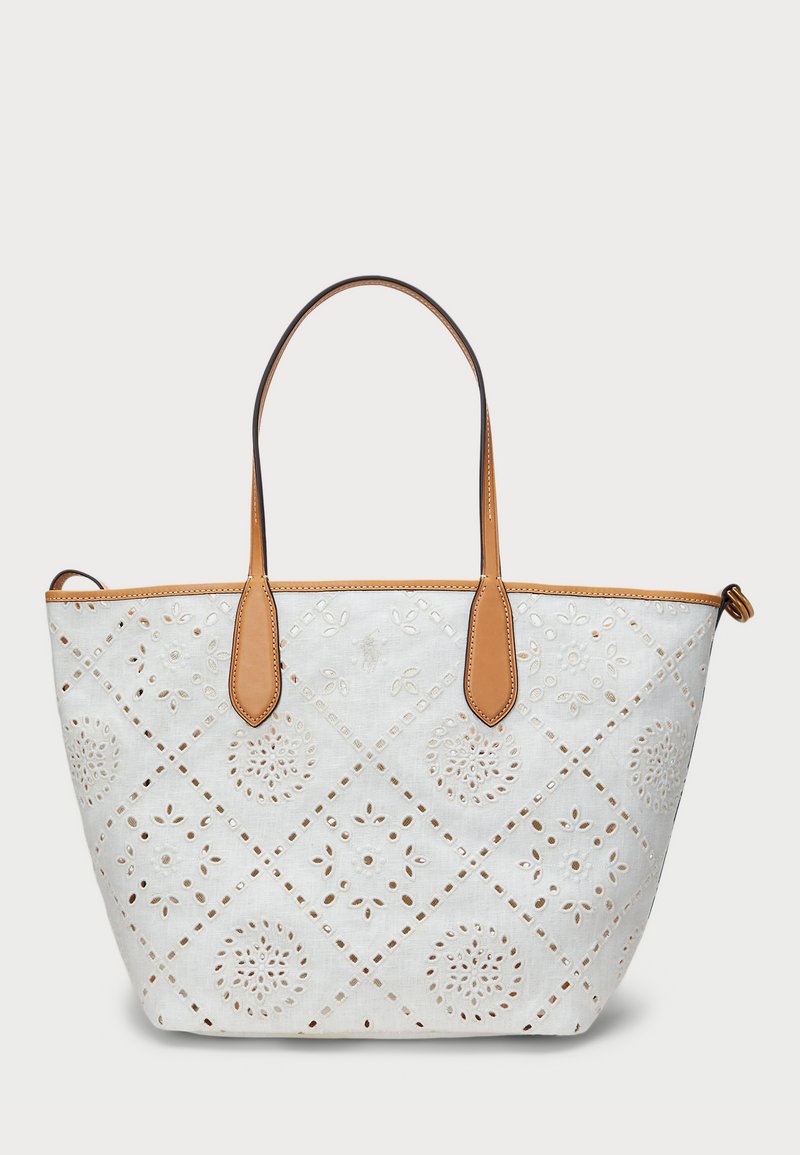 White tote bag with cut-out floral patterns, tan leather accents, and two handles. Diameter of cut-outs features a diamond design.