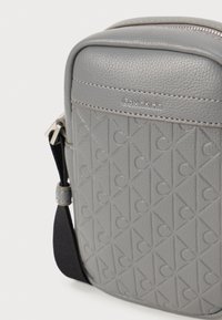Borsa a tracolla in pelle grigia con motivo embossato, chiusura con zip, texture liscia, logo Calvin Klein e tracolla regolabile.